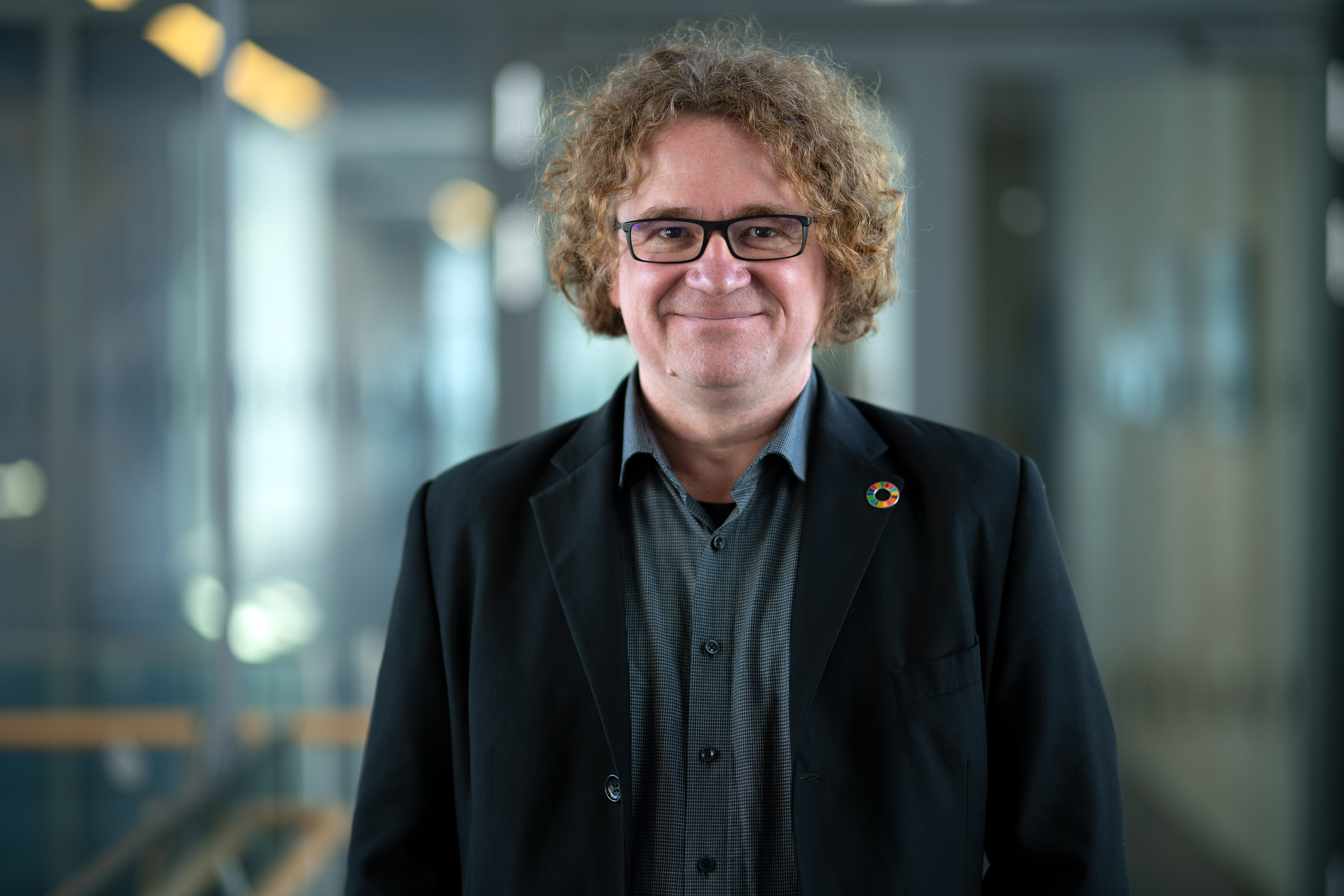 Foto: Prof. Dr. Uwe Handmann lächelt in die Kamera. Er hat dunkelblondes etwas längeres, lockiges Haar und eine Brille mit schwarzem Gestell.