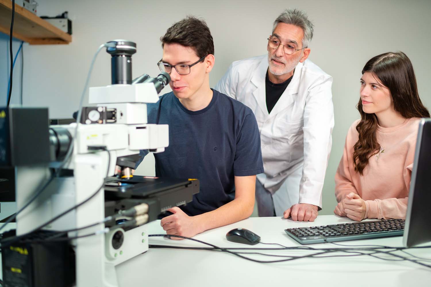 Zwei Studierende und ein Professor arbeiten an einem Mikroskop